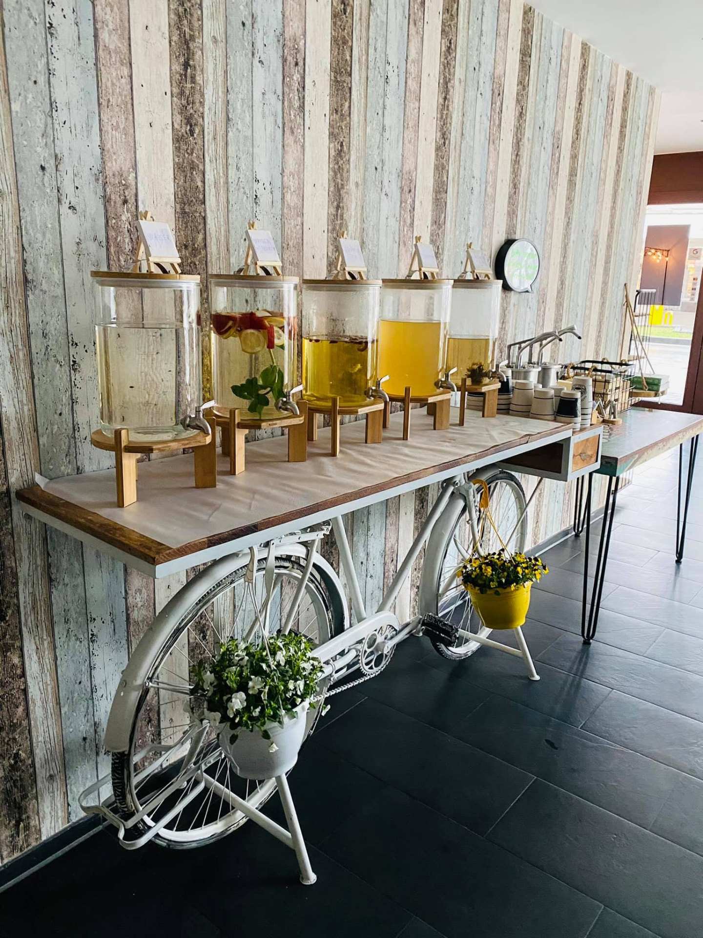 Weißes Fahrrad als Ständer für Limonadenspender an einer Holzwand